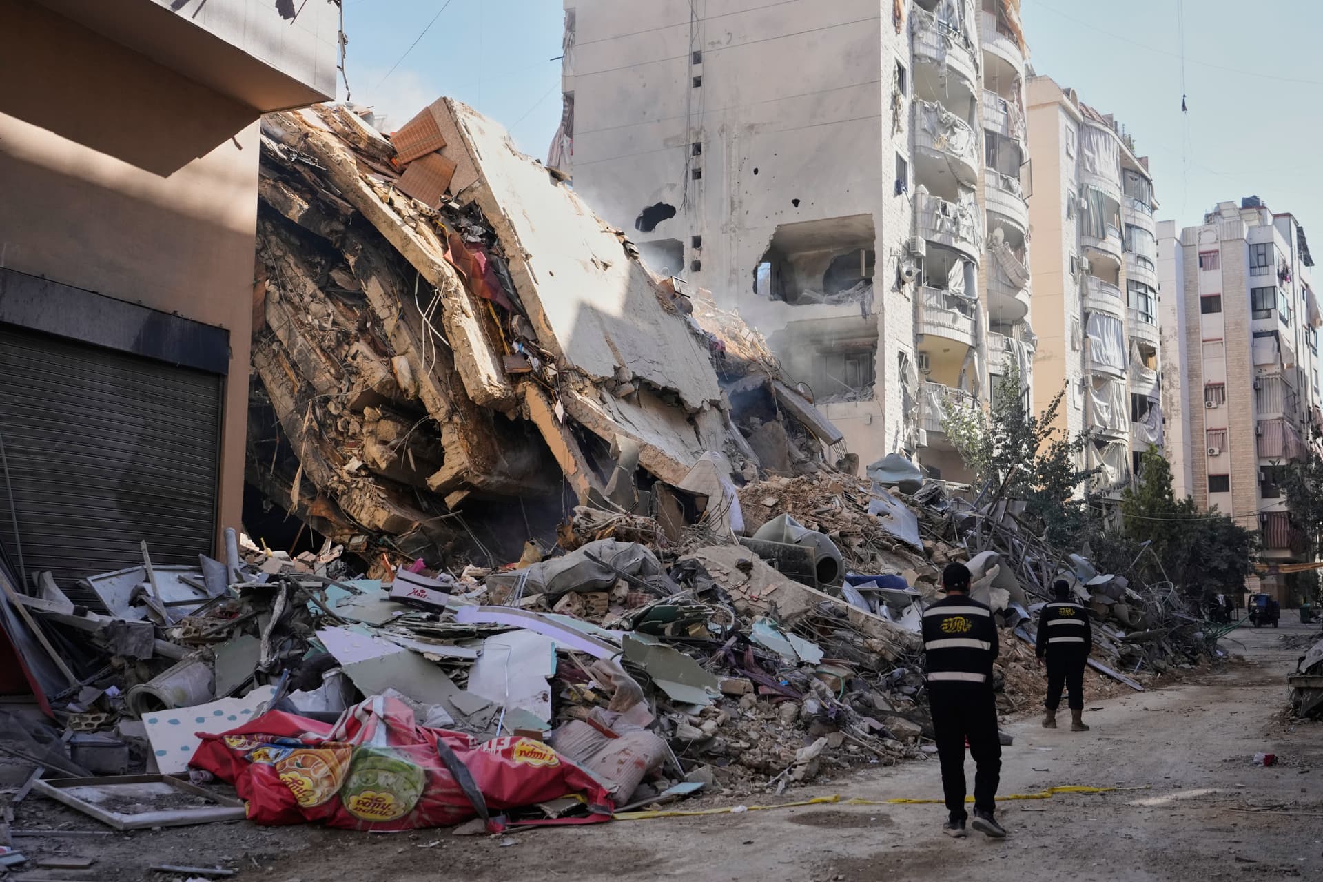 AP/Hassan Ammar Hezbollah members walk past a building destroyed by an Israeli airstrike in Dahiyeh, Beirut's southern suburbs, Lebanon, March 5, 2026.