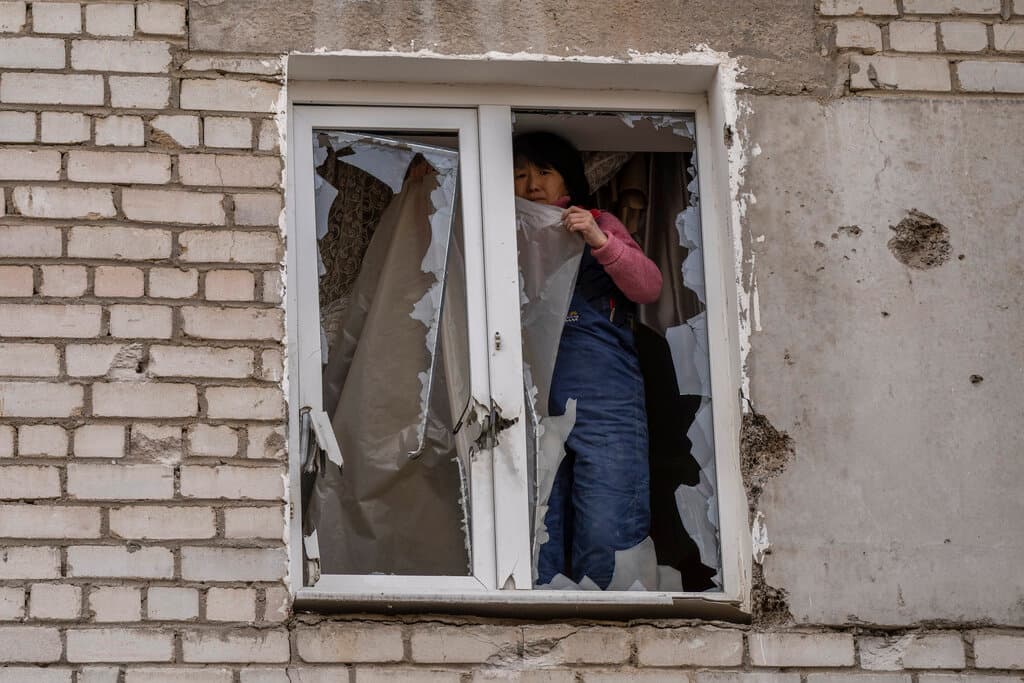 A woman places plastic over her damaged window after a Russian attack at Mykolaiv March 29, 2022. AP/Petros Giannakouris