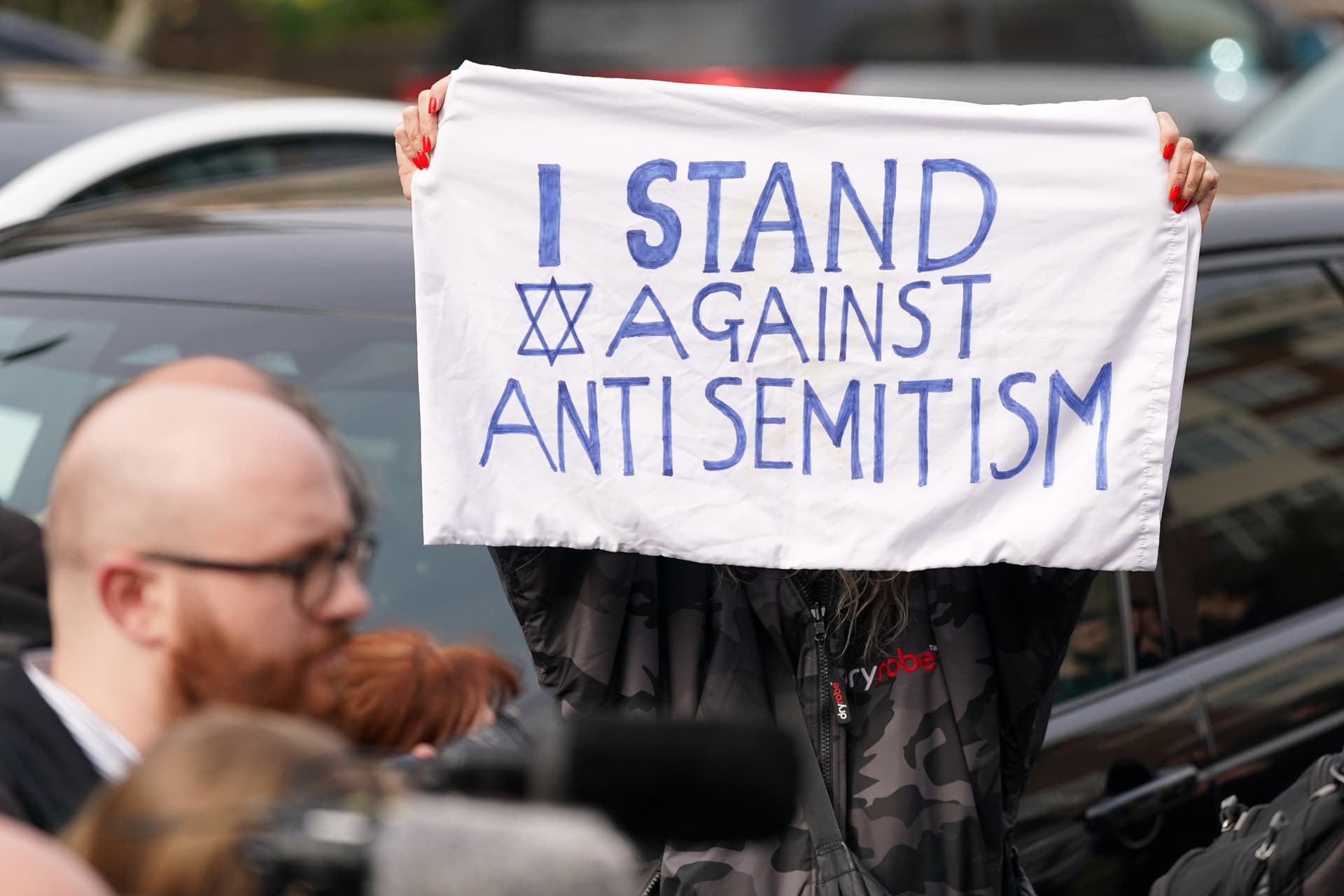 AP/Alberto Pezzali A protester shows a banner at Golders Green in London, Monday, March 23, 2026 after an apparent arson attack on four vehicles belonging to a Jewish ambulance service, Hatzola Northwest, in London.