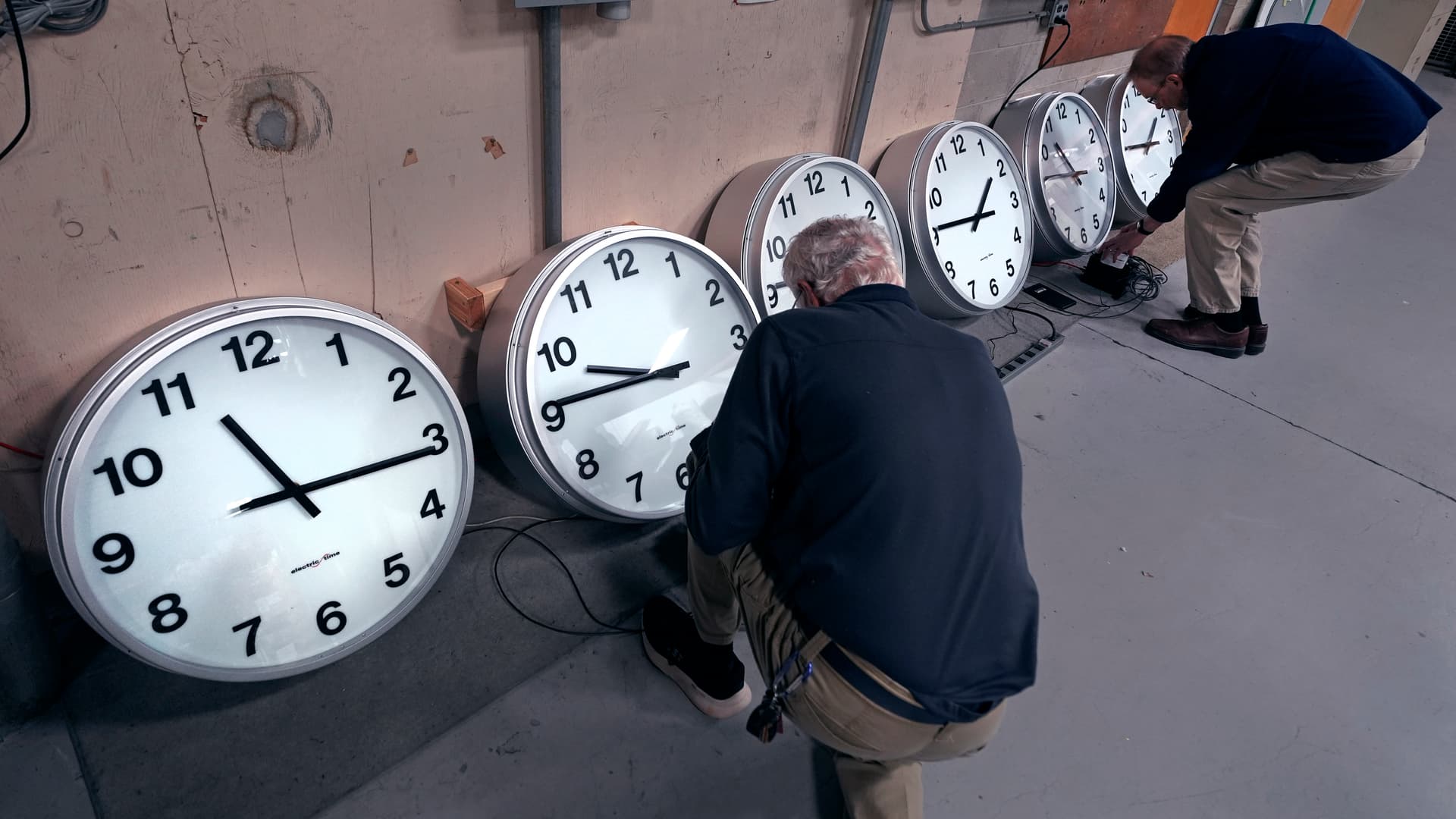 AP/Charles Krupa Clockmakers Rich Finn, left, and Tom Erb adjust the time zone controllers on a series of clocks for Paine Field at Everett, Washington a few days before Daylight Saving 2024.