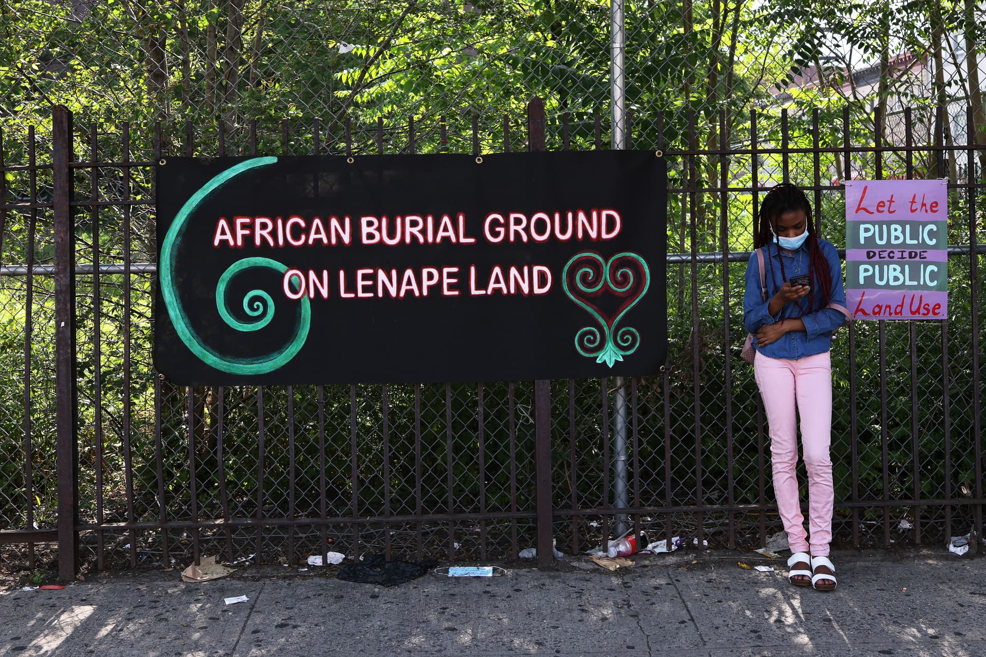Michael M. Santiago/Getty Images A young girl leans next to banners on a fence blocking a lot believed to be a burial ground for enslaved Africans at the Flatbush neighborhood of Brooklyn, New York, on June 9, 2021.