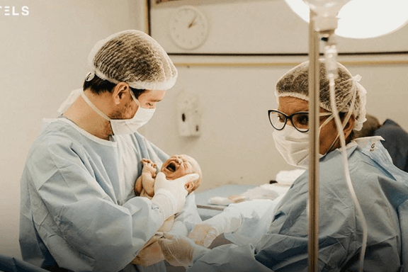 Via X A surgeon and a medical assistant examine a crying, newly born infant. Growing numbers of American parents are refusing an injection of vitamin K routinely provided at birth.