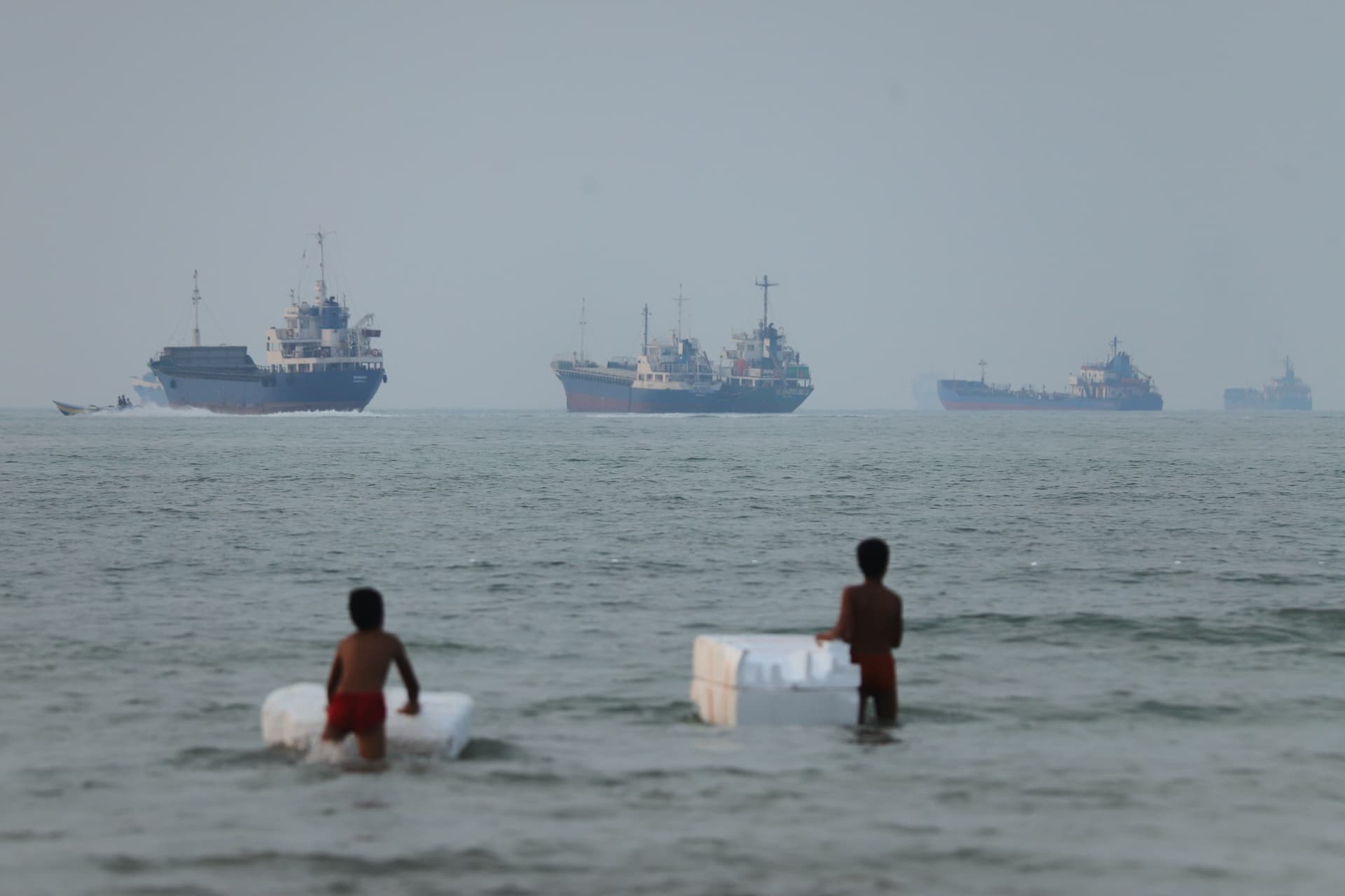 Amirhosein Khorgooi/ISNA via AP Two boys stand play with foam floats as cargo ships and other vessels are seen in the Strait of Hormuz off Bandar Abbas, Iran, on June 30, 2026.