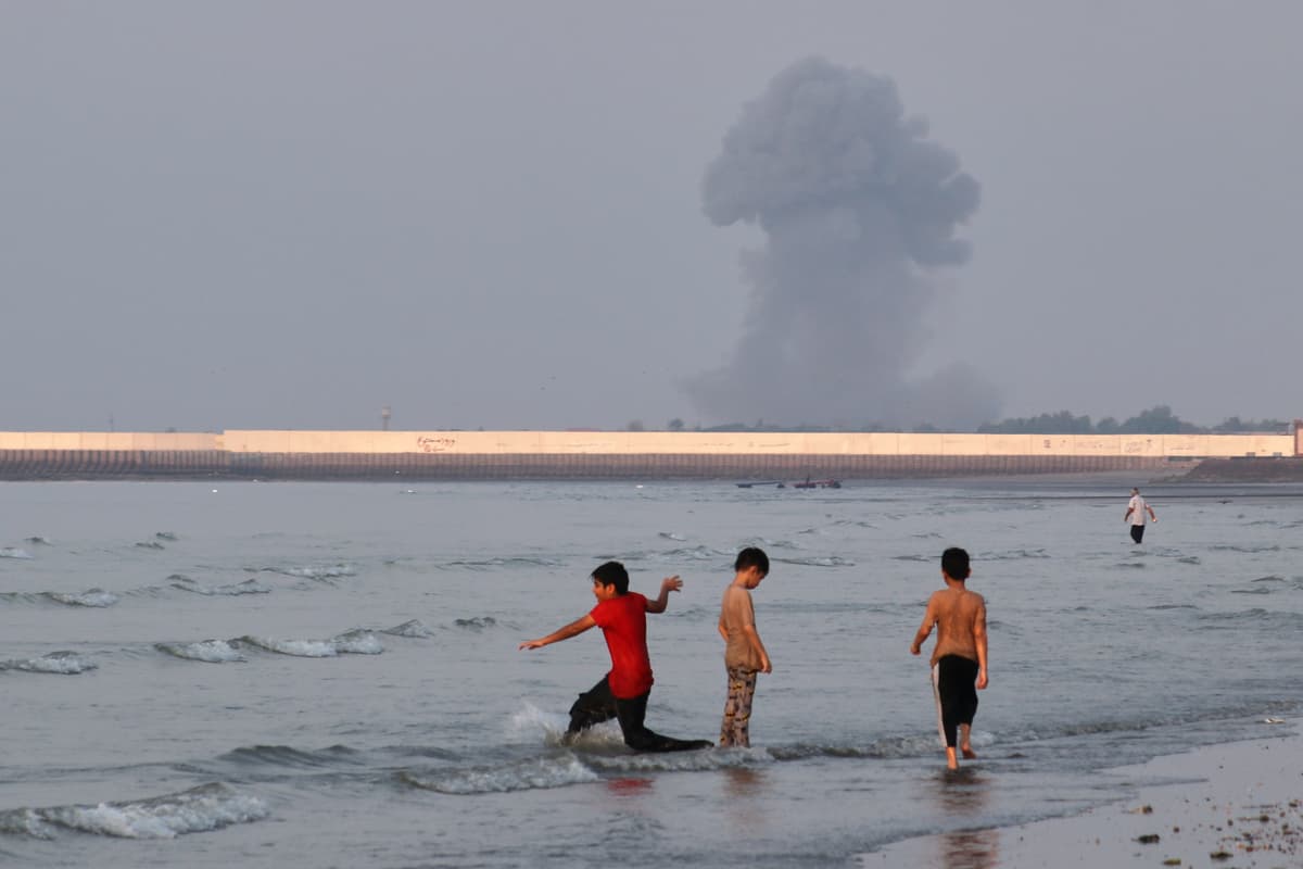 Razieh Poudat/ISNA via AP Three boys play in the shallow waters of the Strait of Hormuz, as a plume of smoke rises from an explosion in the background, off Bandar Abbas, Iran, July 13, 2026.