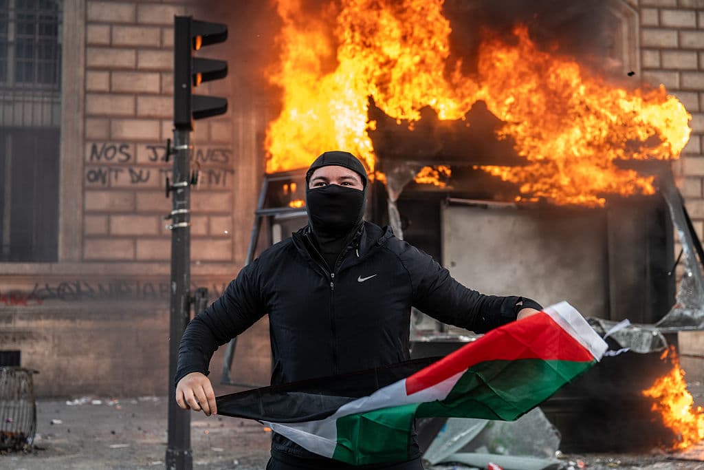 A protester holds a Palestinian flag as a bus stop burns at Paris, France. A protester holds a Palestinian flag as a bus stop burns at Paris, France.